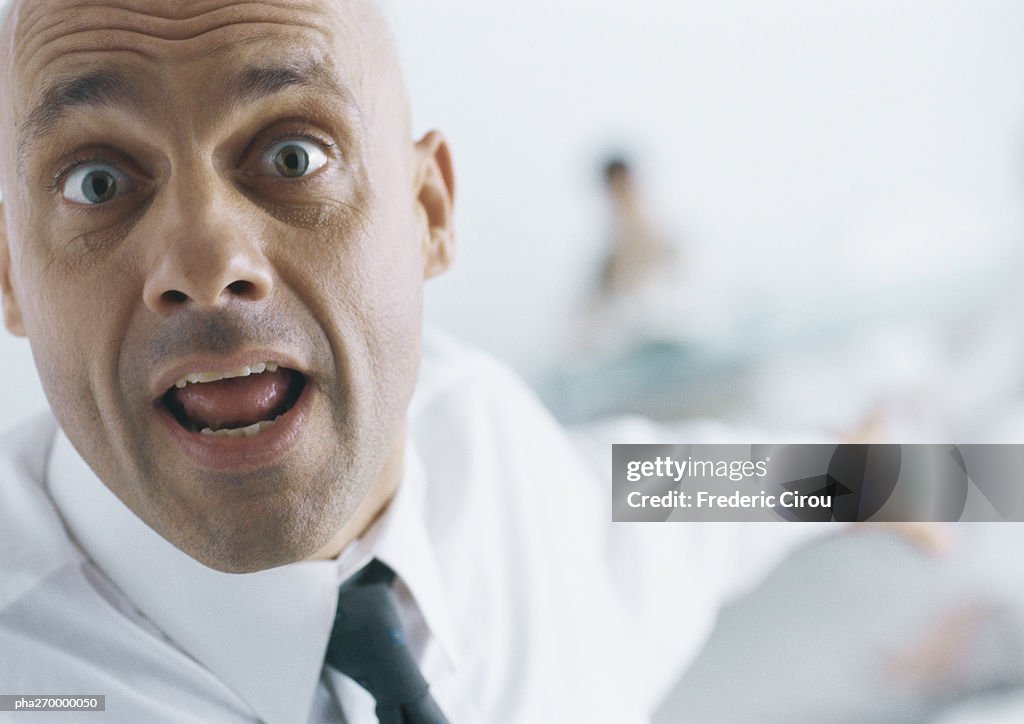 Businessman with eyebrows raised and mouth open pointing into background, close-up