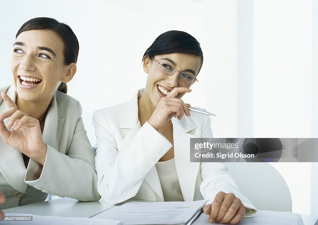 Two businesswomen laughing, looking to the side