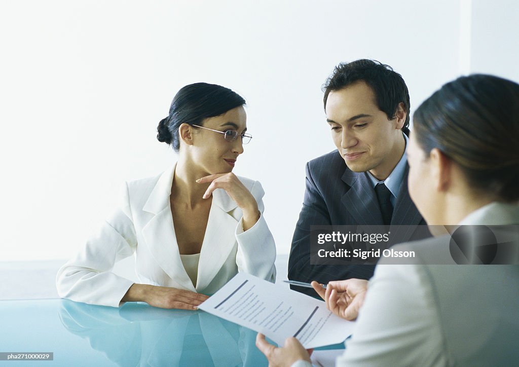 Businessman and businesswoman sitting at table across from businesswoman holding out document and pen