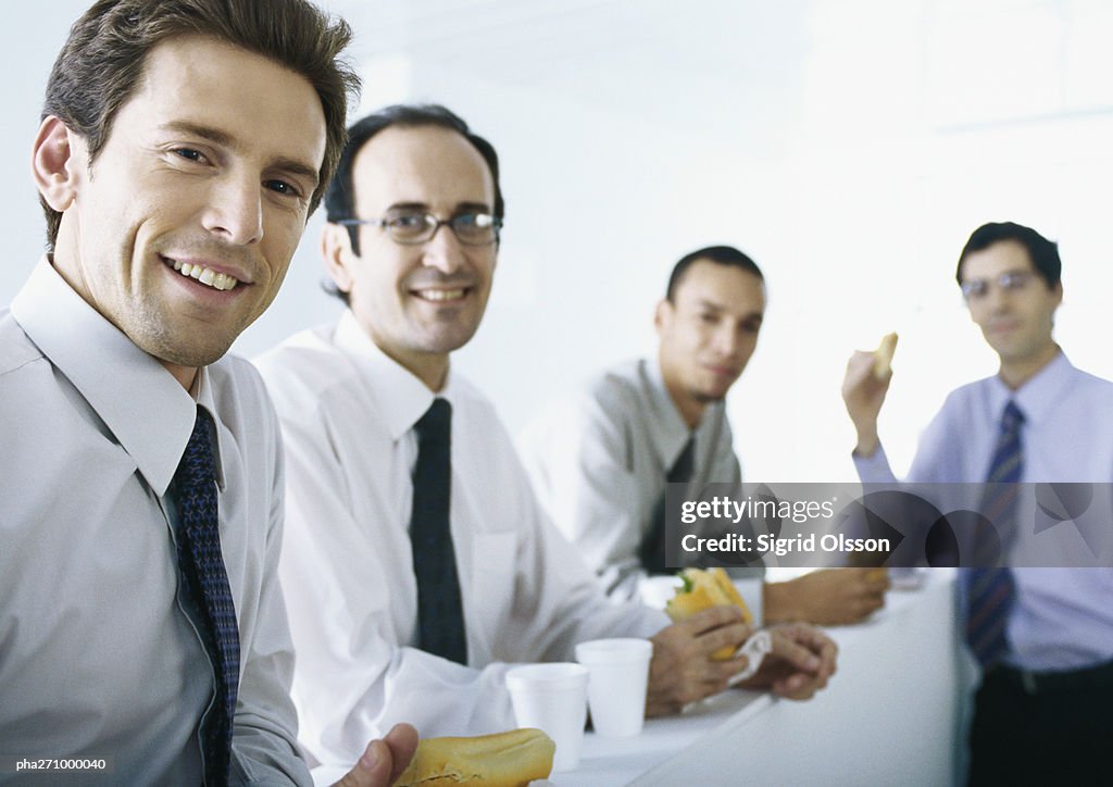 Businessmen standing around counter with food and drinks