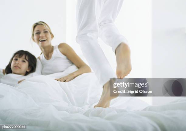 boy jumping on bed, woman and girl in bed in background - girls wrestling stock pictures, royalty-free photos & images