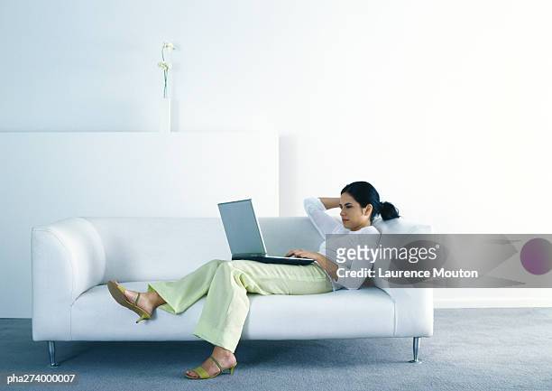woman lounging on sofa and using laptop - achterover leunen stockfoto's en -beelden