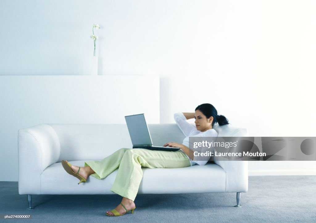 Woman lounging on sofa and using laptop