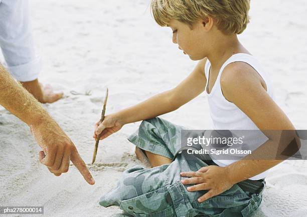 boy sitting on sand, drawing with stick, father pointing - stick plant part stockfoto's en -beelden