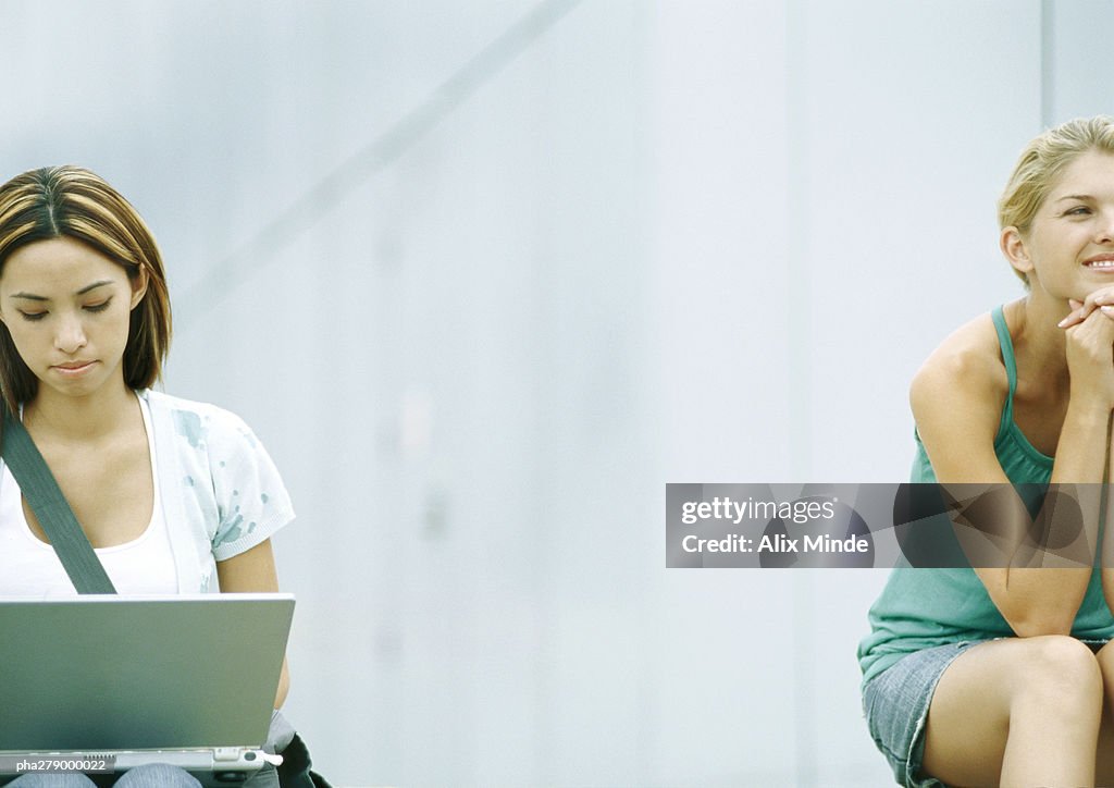 Two students sitting outdoors, one using laptop