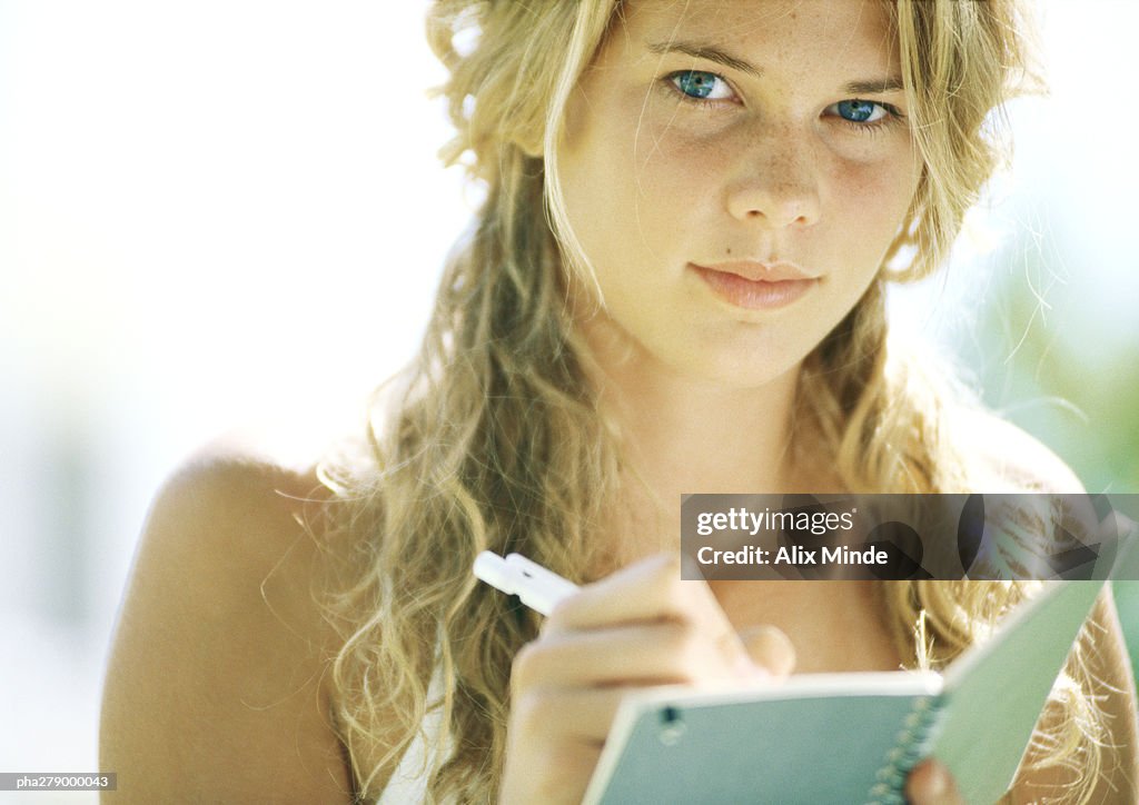 Female student writing in notebook, looking at camera, close-up