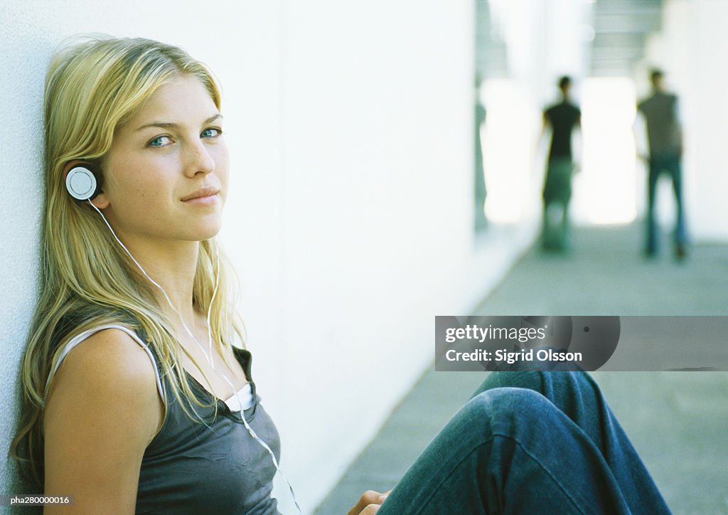 Young woman listening to headphones, looking at camera