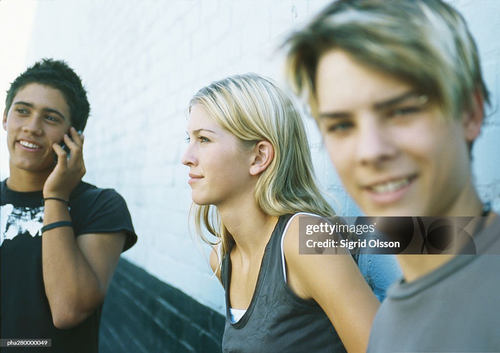 Young people standing next to wall, one using cell phone