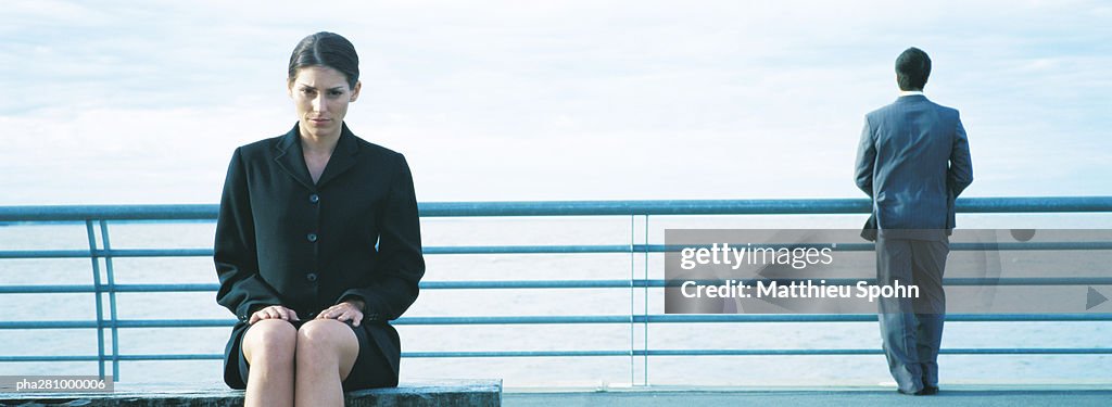 Businesswoman sitting, businessman standing at railing in background, panoramic