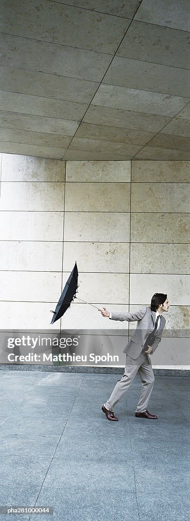 Businessman walking forward, holding umbrella inside out behind him