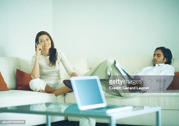 man and woman sitting on couch, man reading while woman uses cell phone - gerrard stock-fotos und bilder