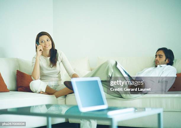 man and woman sitting on couch, man reading while woman uses cell phone - uses stock pictures, royalty-free photos & images