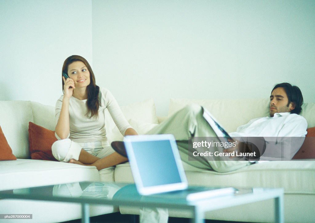 Man and woman sitting on couch, man reading while woman uses cell phone