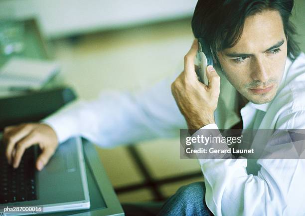 man using laptop and cell phone, looking over shoulder - gerrard stock-fotos und bilder