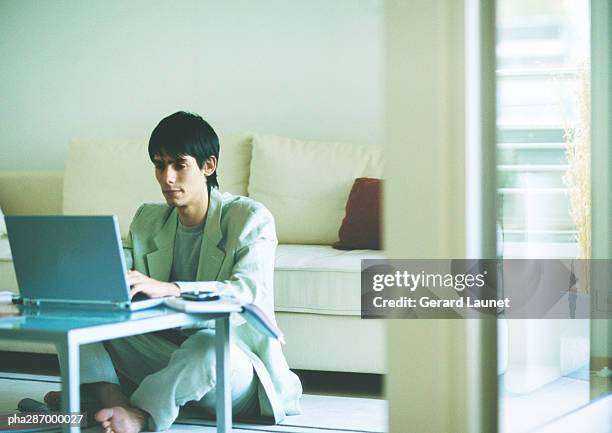 young man sitting on floor, using laptop on coffee table - gerrard stock-fotos und bilder