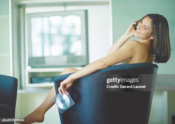 woman sitting in chair, using cell phone and holding cd - gerrard stock-fotos und bilder