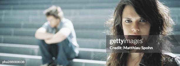 young woman looking at camera, young man sitting in background - kommunikationsproblem stock-fotos und bilder