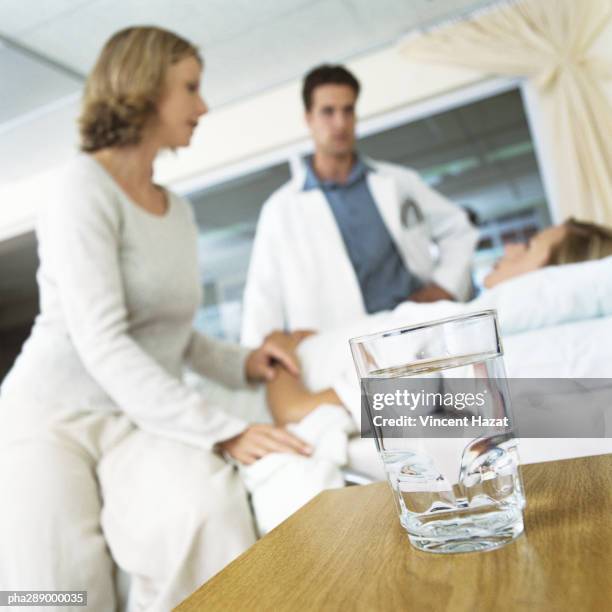 glass of water on table and patient receiving visit from male doctor and woman - rapporto medico paziente foto e immagini stock