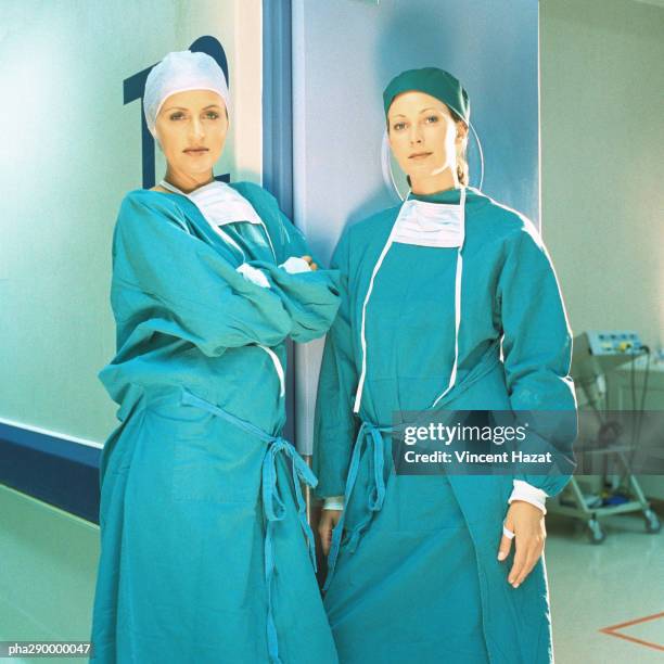 two female doctors in operating gowns, leaning against doorframe - chirurgenkappe stock-fotos und bilder