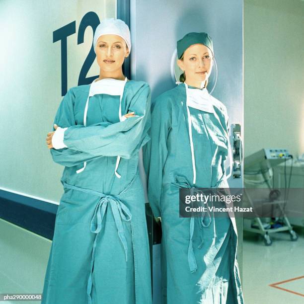 two female doctors in operating gowns, leaning against doorframe - operatiegewaad stockfoto's en -beelden