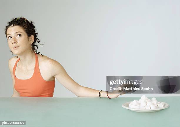 young woman reaching toward plate of marshmallows - couvert stock pictures, royalty-free photos & images