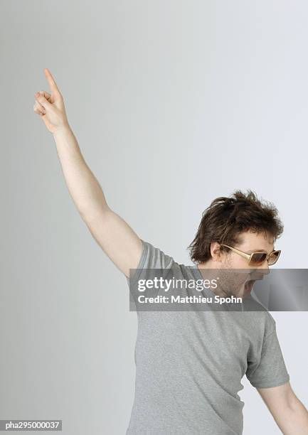 young man with hand up in air and mouth open, wearing sunglasses, portrait - open arms stock-fotos und bilder