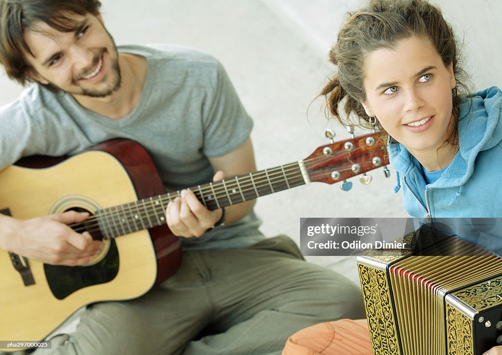 Young man playing guitar, young woman playing accordion