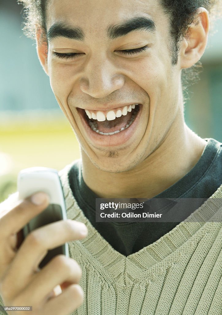 Young man laughing and looking at cell phone, close-up