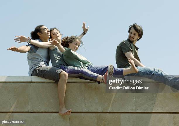 young people sitting on top of wall with arms out - frau lachen profil stock-fotos und bilder