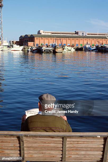 spain, barcelona, man sitting on bench reading newspaper by the water - former chief of catalan police attends to spain national court stockfoto's en -beelden