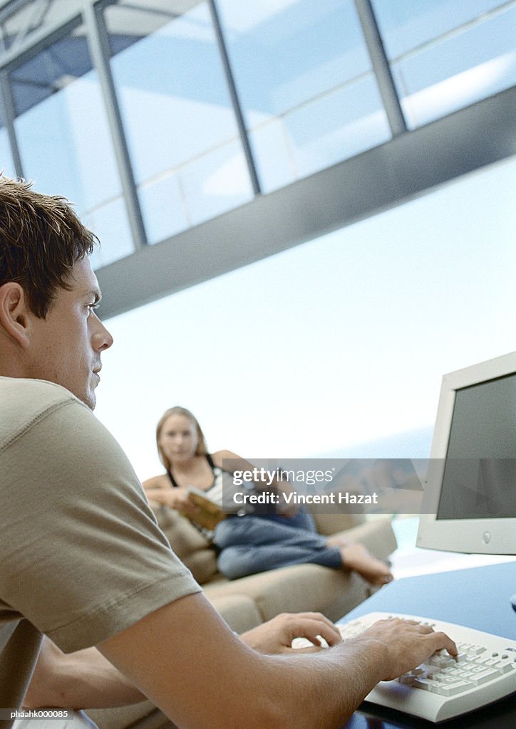 Man using computer, woman sitting on sofa in background