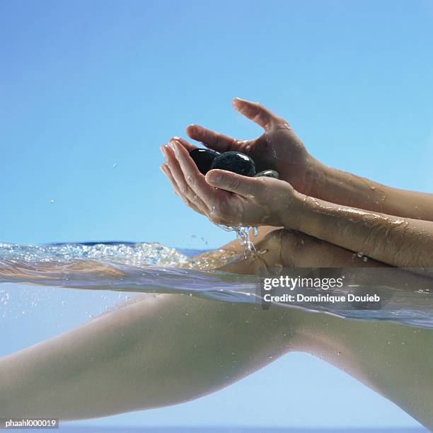 woman sitting in water holding stones, close up of legs and hands - balneotherapy stock pictures, royalty-free photos & images