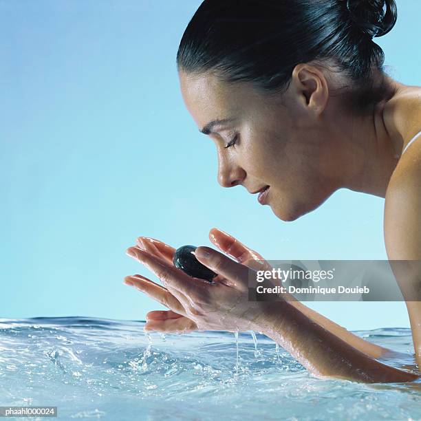 woman in water holding stones in hands with eyes closed, side view - balneotherapy stock pictures, royalty-free photos & images
