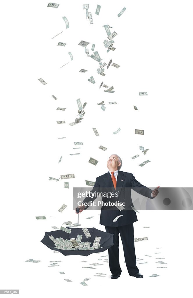 Conceptual photo of a caucasian man in a suit standing in raining money and catches it in umbrella