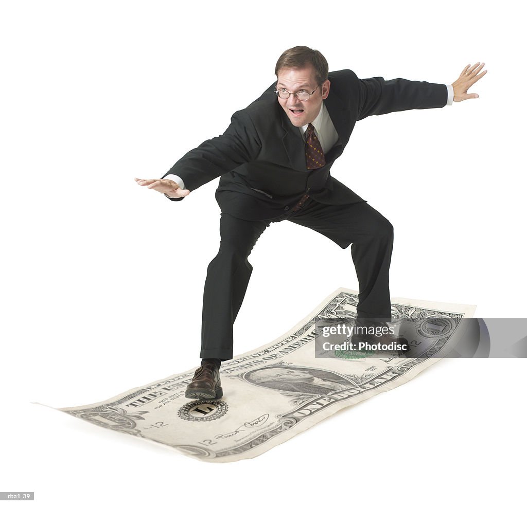 Conceptual photo of a caucasian business man in a suit as he playfully surfs on a dollar bill