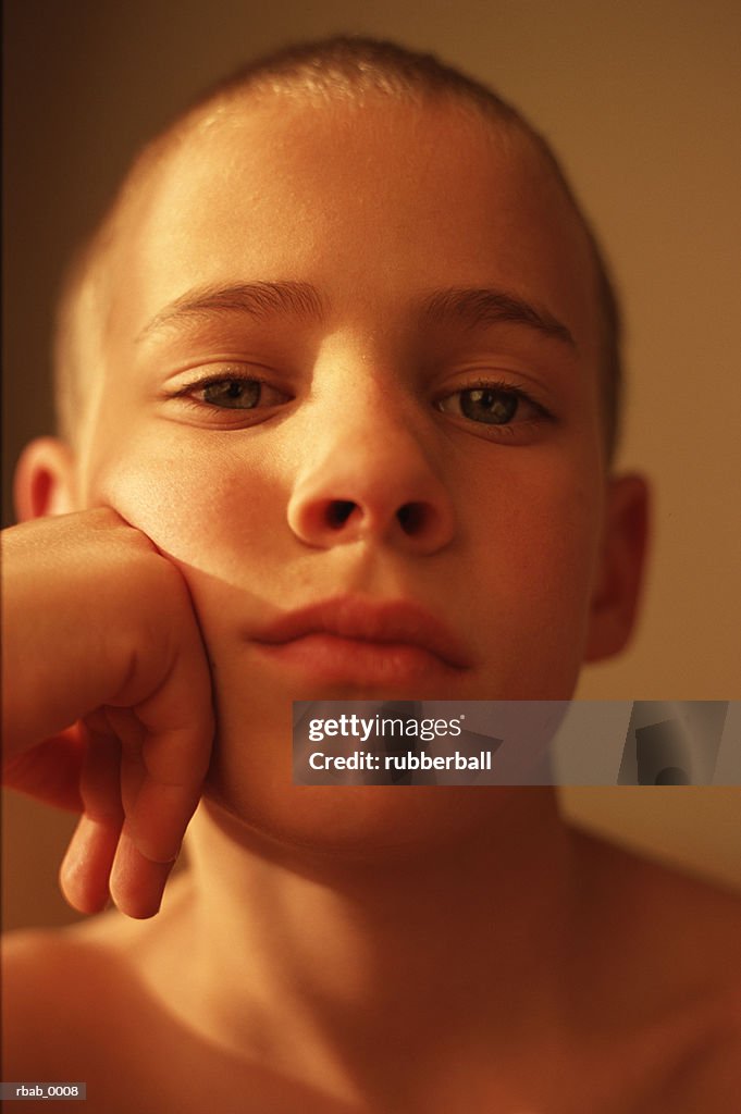 A young man is looking into the camera with his face resting on his hand