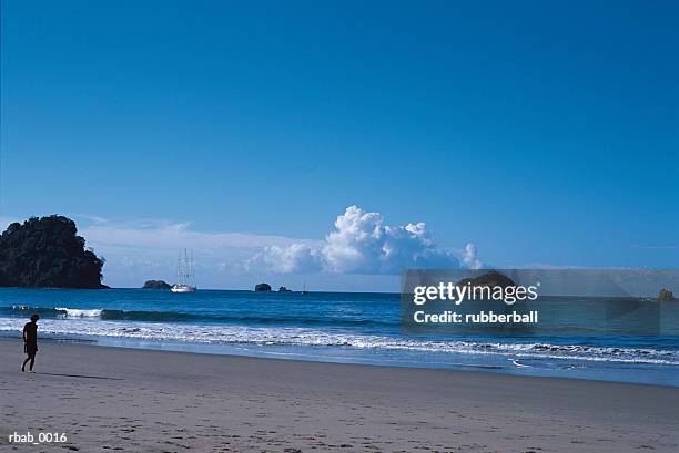 a man is walking along a stretch of beach with a blue ocean and a sailboats in the background in costa rica - costa stock pictures, royalty-free photos & images