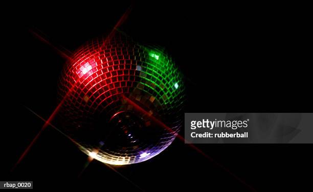 a red and green spotlighted disco ball hangs in a darkened dance room - disco ball foto e immagini stock