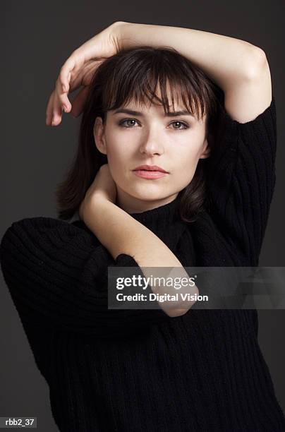 a young caucasian brunette in a black turtleneck sweater raises her arms up and around above her head - turtleneck stock pictures, royalty-free photos & images