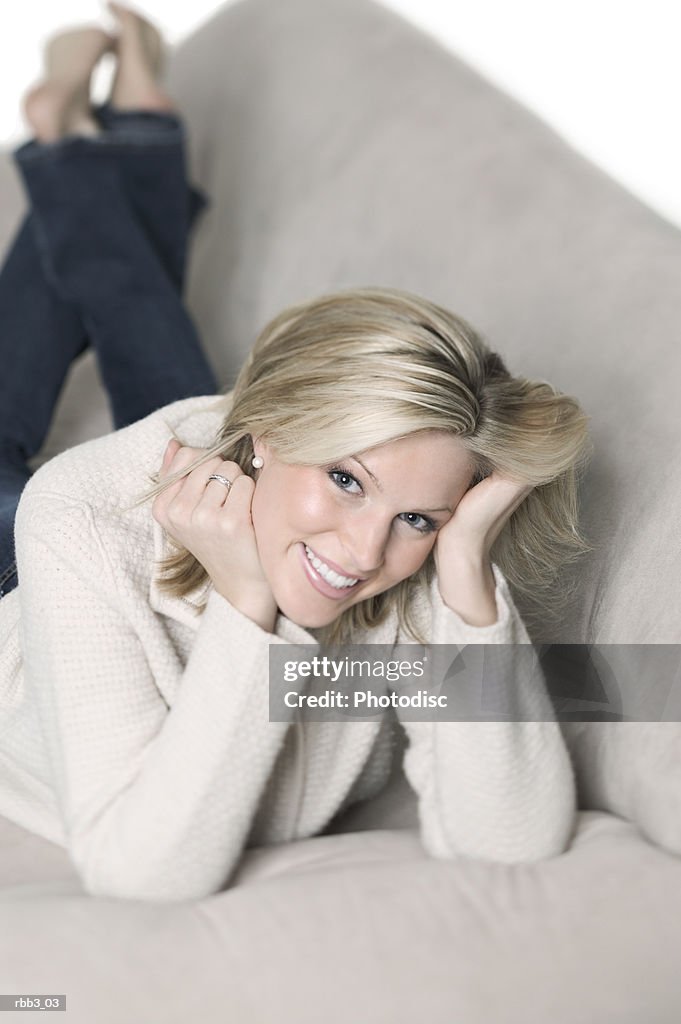 A young blonde caucasian woman lays on a couch and smiles