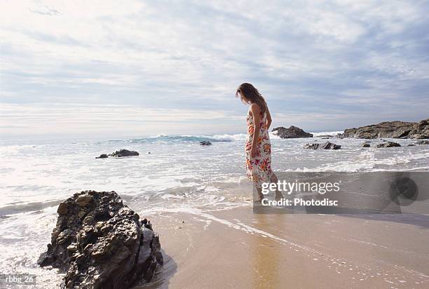 girl in dress walking along the beach on a cloudy afternoon - ankle deep in water stock pictures, royalty-free photos & images