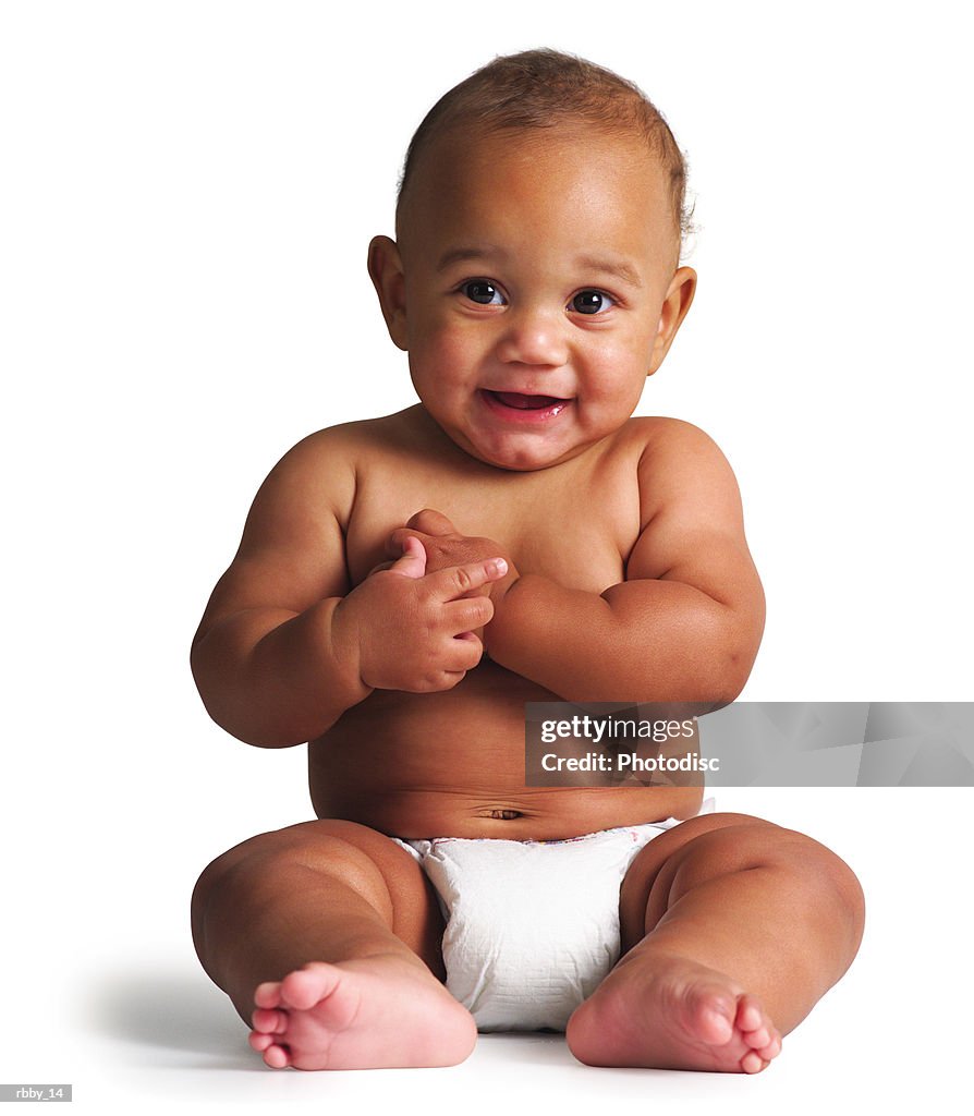 An african american baby sits in a diaper and smiles slightly