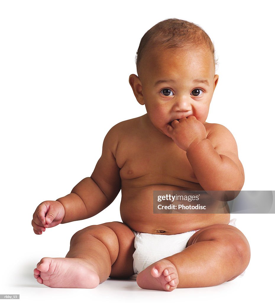 An african american baby sits in a diaper and puts his hand in his mouth