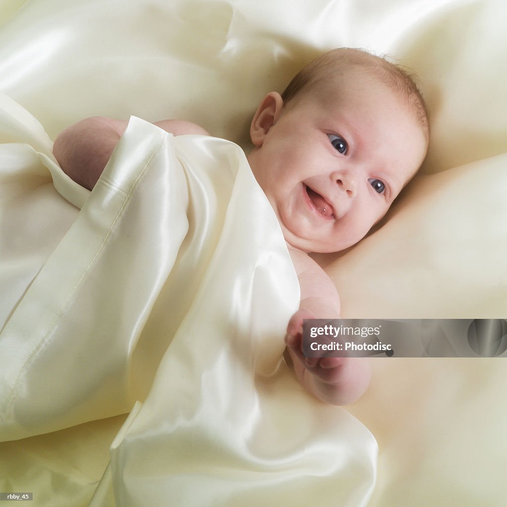 A caucasian baby lies on its back wrapped in sheets