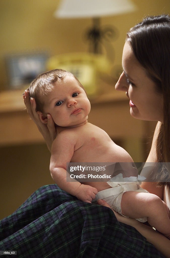 A young caucasian mother holds her newborn baby out as she smiles at it