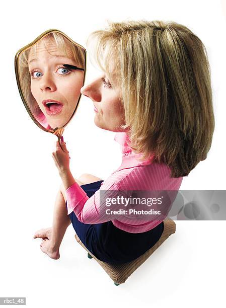 photo caricature of a blonde caucasian woman in a pink blouse as she sits down and applies mascara as she looks into a mirror - down blouse ストックフォトと画像