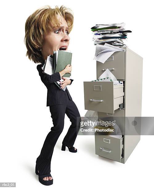 a caucasian woman holding a stack of files stands in front of an overfilled file cabinet looking overwhelmed at all of the papers - file cabinet stock-fotos und bilder