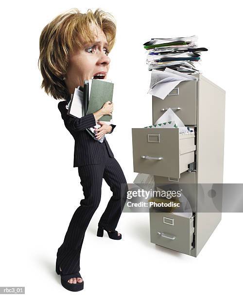 a caucasian woman holding a stack of files stands in front of an overfilled file cabinet looking overwhelmed at all of the papers - all stock pictures, royalty-free photos & images