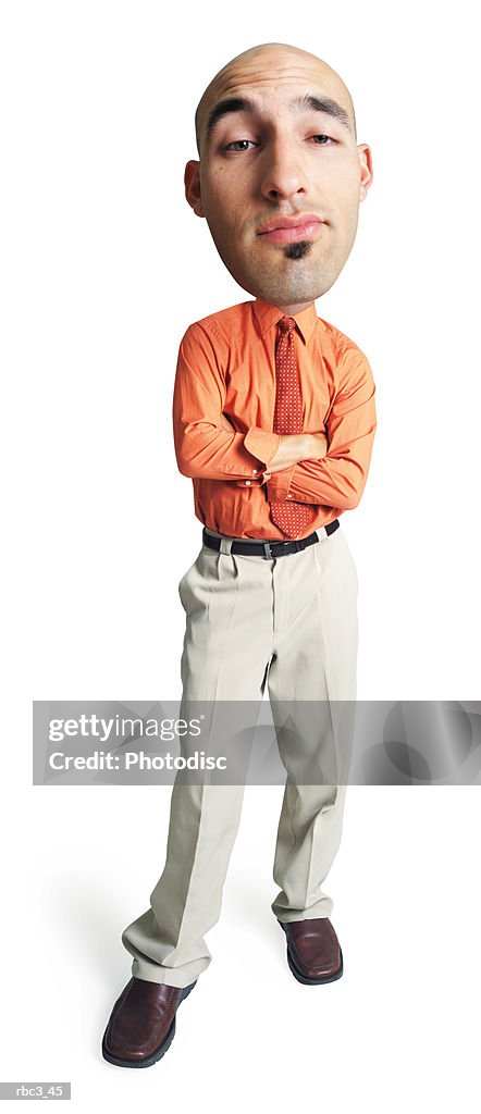 A young caucasain bald male in tan pants and an orange shirt folds his arms and looks smugly into the camera