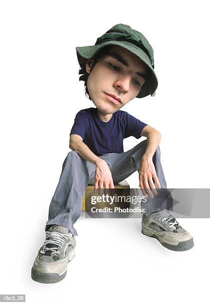 a young caucasian male wearing a khaki fisherman hat sits on a small box and rests his arms on his knees while looking pensively at the ground - thinking out of the box bildbanksfoton och bilder